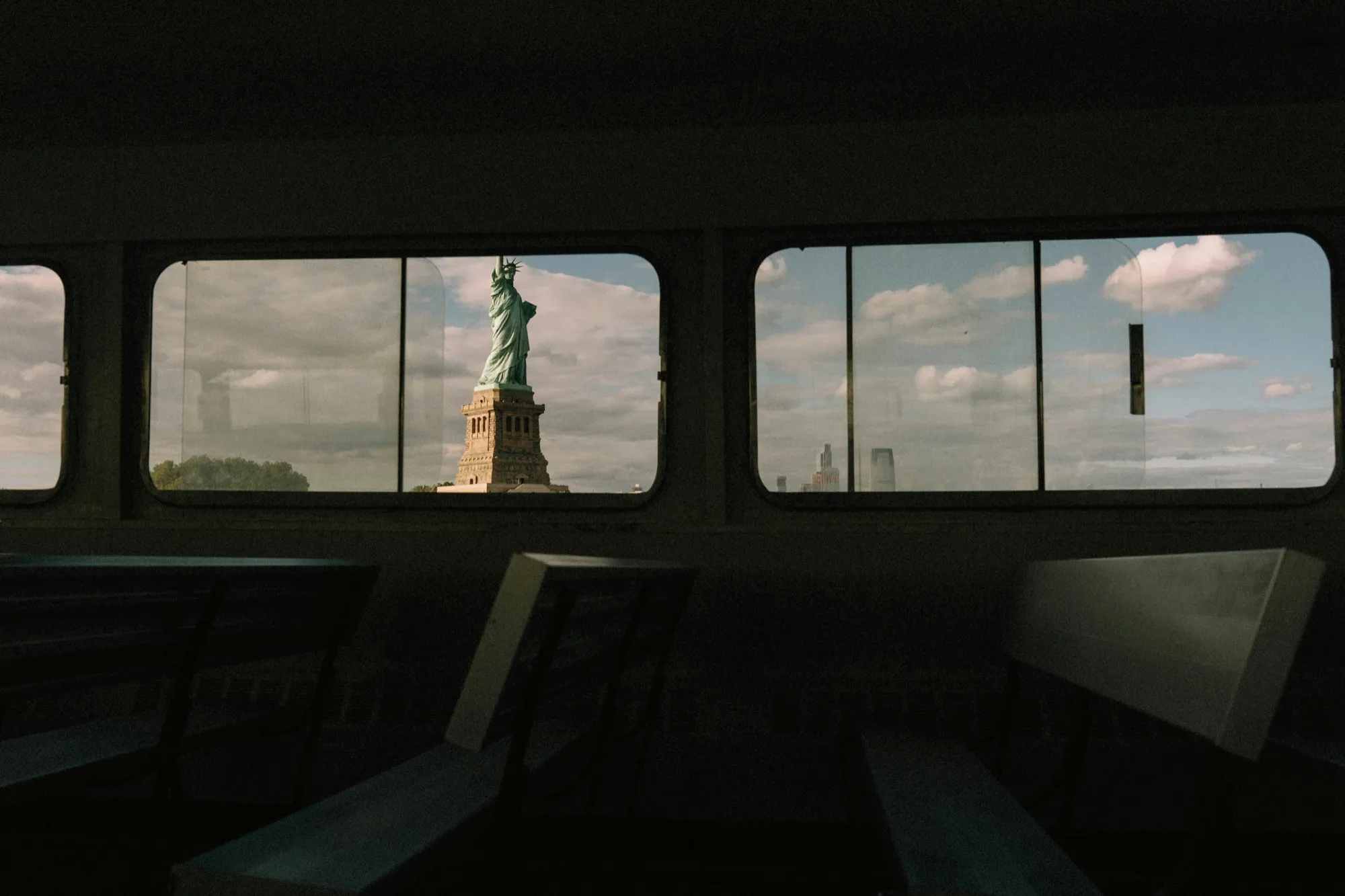 The Statue of Liberty through the windows of a ferry, benches in the foreground